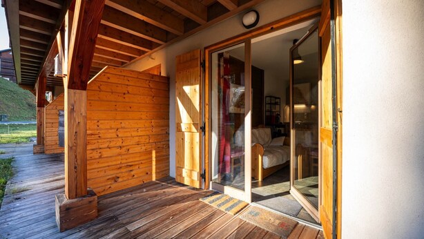 A wooden exterior with a covered porch and a sliding glass door leading to a bedroom.