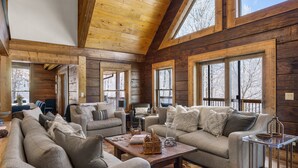 A spacious living room with a high ceiling and large windows, furnished with sofas and a coffee table. - 5BR Lodge w/ Hot Tub, Game Room, Great Views & Pet-Friendly (Banner Elk)
