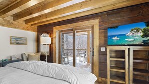 A bedroom with a large bed, wooden ceiling beams, a TV, and a balcony with a view of boats and trees. - 5BR Lodge w/ Hot Tub, Game Room, Great Views & Pet-Friendly (Banner Elk)