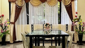 A dining area with a glass table surrounded by chairs, a vase with flowers, and curtains with tassels. - South Villa Apartelle Panglao Bohol (Panglao)