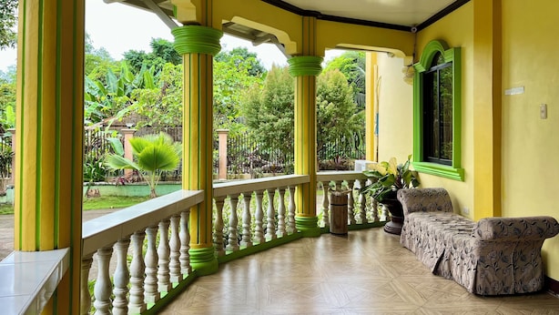A covered porch with yellow walls and green columns, a wooden floor, and a sofa. - South Villa Apartelle Panglao Bohol (Panglao)