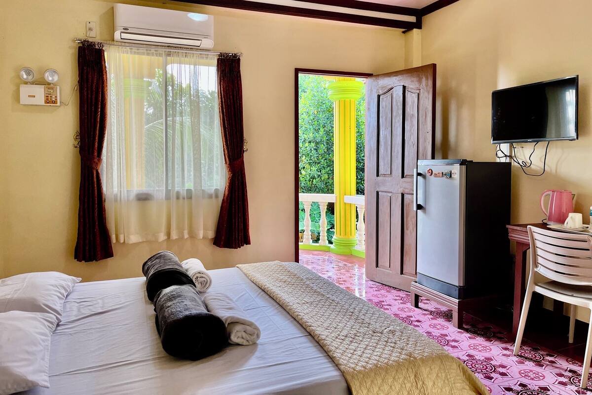 A hotel room with a bed, a TV, a refrigerator, and a window with curtains.