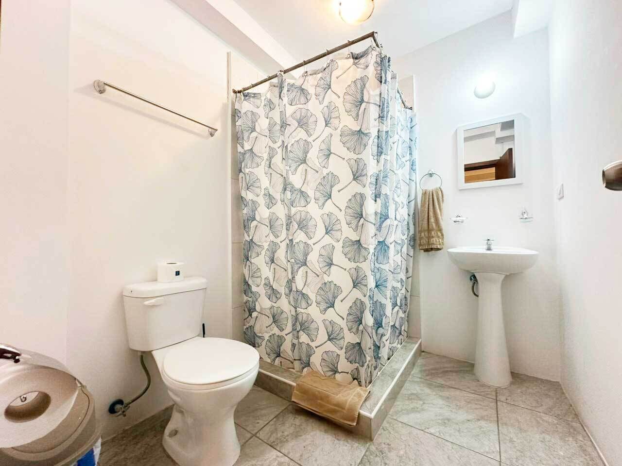 A bathroom with a toilet, shower curtain, sink, and a towel rack.