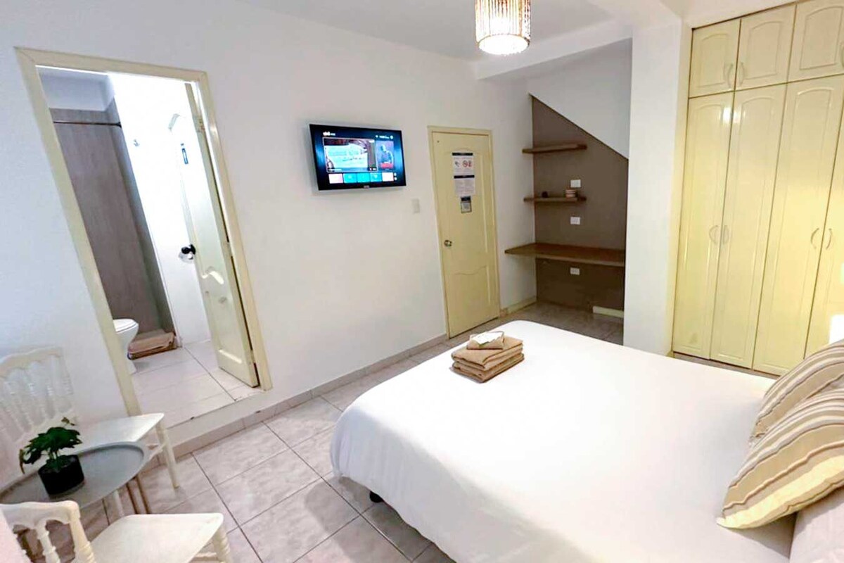 A hotel room with a bed, a TV, a wardrobe, a desk, and a chair.