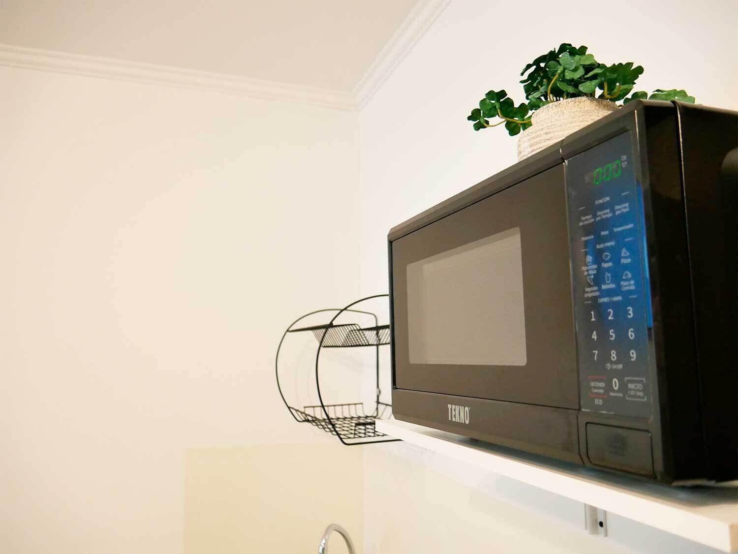 A microwave oven on a white shelf with a plant on top.