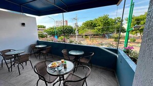 A covered outdoor seating area with tables and chairs, a view of the street, and a balcony with plants. - Park View Hostel & Suites (Manta)