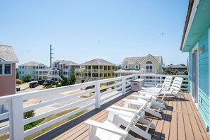 A wooden deck with white chairs and a white fence overlooking a row of houses. - A Bbitt Beachy: Oceanside, Hot Tub, Community Pool, Easy Beach Access (Nags Head)