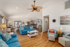 Un amplio espacio de sala con un sofá azul, una mesa de centro blanca y un ventilador de techo.