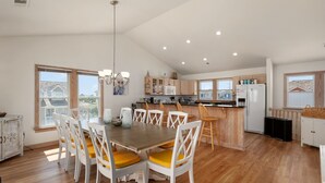A spacious kitchen with wooden cabinets, a central island, and a dining area with a table and chairs. - A Bbitt Beachy: Oceanside, Hot Tub, Community Pool, Easy Beach Access (Nags Head)
