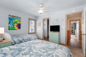 A bedroom with two beds, a ceiling fan, a TV, and a painting. - A Bbitt Beachy: Oceanside, Hot Tub, Community Pool, Easy Beach Access (Nags Head)