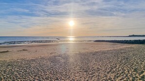 A beach with a clear sky and the sun setting over the horizon.