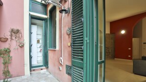 A hallway with a pink wall, green shutters, and a tiled floor.