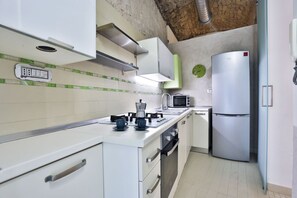 Una cocina con armarios blancos, un microondas, un refrigerador y una cafetera.