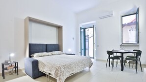 A modern bedroom with a bed, bedside table, and a dining area with chairs.