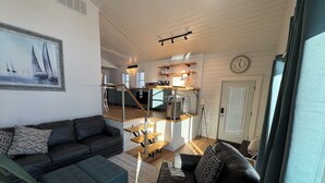 A modern living room with a sofa, ottoman, and a staircase leading to a kitchen area. - Charming log cabin (Spring Lake)