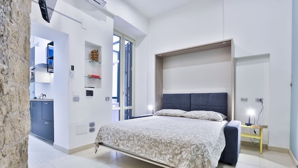 Un dormitorio con cama, mesita de noche y vista a la cocina.