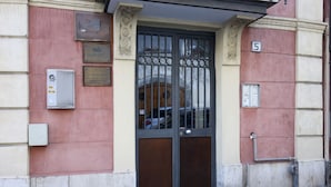 Entrada de un edificio con una reja de metal, una placa y un cuadro eléctrico.
