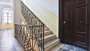 Una escalera con barandillas de metal ornamentadas, una puerta de madera oscura y un suelo de baldosas.