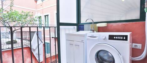 A laundry area with a washing machine, a sink, and a balcony with a view of a building.