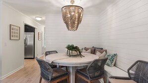 A dining area with a round table, wicker chairs, a chandelier, and a refrigerator in the background. - Pool View! Dog-friendly | Easy Walk to Beach, Restaurants, Village, and Pier. (Saint Simons Island)