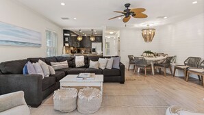 A modern living room with a dark brown sectional sofa, a white coffee table, and a dining area with wicker chairs and a wooden table. - Pool View! Dog-friendly | Easy Walk to Beach, Restaurants, Village, and Pier. (Saint Simons Island)