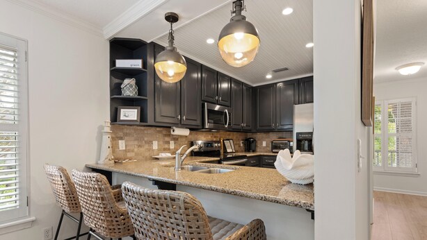 A modern kitchen with dark cabinets, a granite countertop, and a central island with bar stools. - Pool View! Dog-friendly | Easy Walk to Beach, Restaurants, Village, and Pier. (Saint Simons Island)
