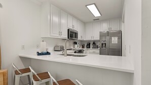 A modern kitchen with white cabinets, stainless steel appliances, and a bar area with stools. - Dog Friendly, Steps away from the beach, Restaurants, Village, and Pier. (Saint Simons Island)