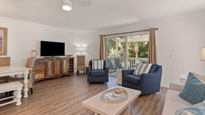 A spacious living room with a large window, a flat-screen TV, and a wooden cabinet. - Dog Friendly, Steps away from the beach, Restaurants, Village, and Pier. (Saint Simons Island)