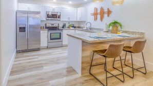 A modern kitchen with white cabinets, stainless steel appliances, a granite countertop, and a bar area with stools. - 8Guest, 5 minutes to everything in Miami (Miami)