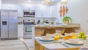 A modern kitchen with white cabinets, stainless steel appliances, and a breakfast setup with plates, bowls, and fruits. - 8Guest, 5 minutes to everything in Miami (Miami)