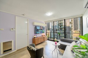 Un salon moderne dotĂ© dâun tĂ©lĂ©viseur Ă Ă©cran plat, dâun canapĂ©, dâune table Ă manger et offrant une vue sur le paysage urbain grĂące Ă de grandes fenĂȘtres.