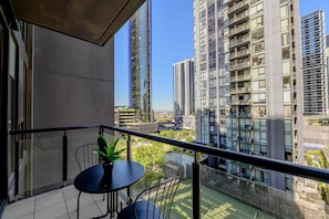 Un balcon avec une table et des chaises, donnant sur un paysage urbain avec de hauts immeubles.