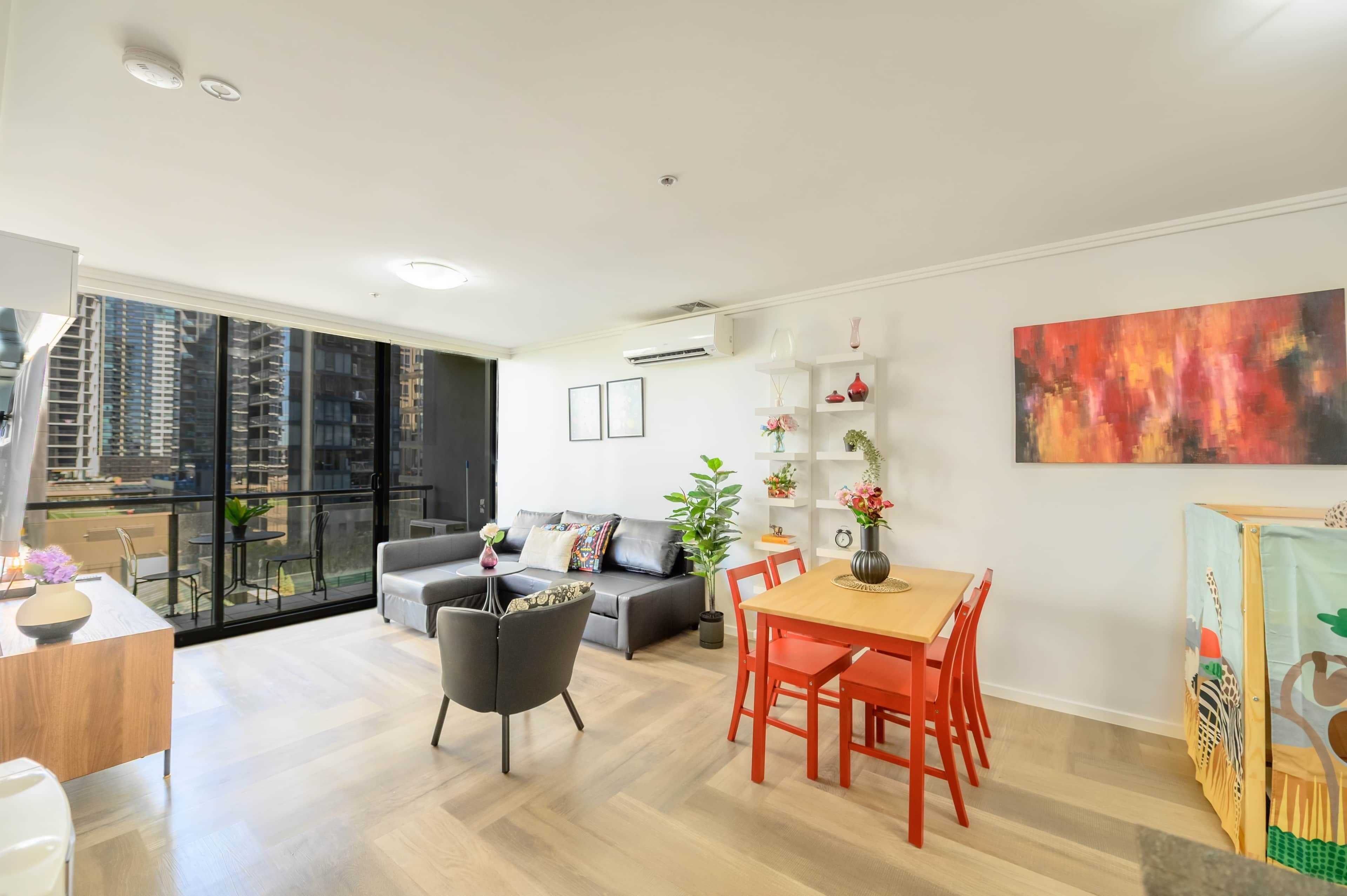 Un salon moderne comprenant un canapé, une table à manger, des chaises et un balcon offrant une vue sur les immeubles de grande hauteur.