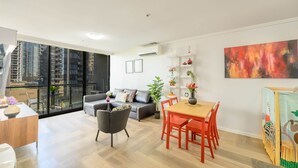 Ein modernes Wohnzimmer mit Sofa, Esstisch, Stühlen und einem Balkon mit Blick auf hohe Gebäude.