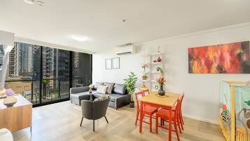 Un salon moderne comprenant un canapé, une table à manger, des chaises et un balcon offrant une vue sur les immeubles de grande hauteur.