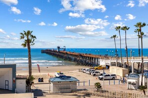 A beachside pier with a bistro, parked cars, and palm trees.