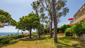 A grassy outdoor area with a swing set, trees, and a building with a balcony. - Boudi..ou by Interhome (Anthéor)