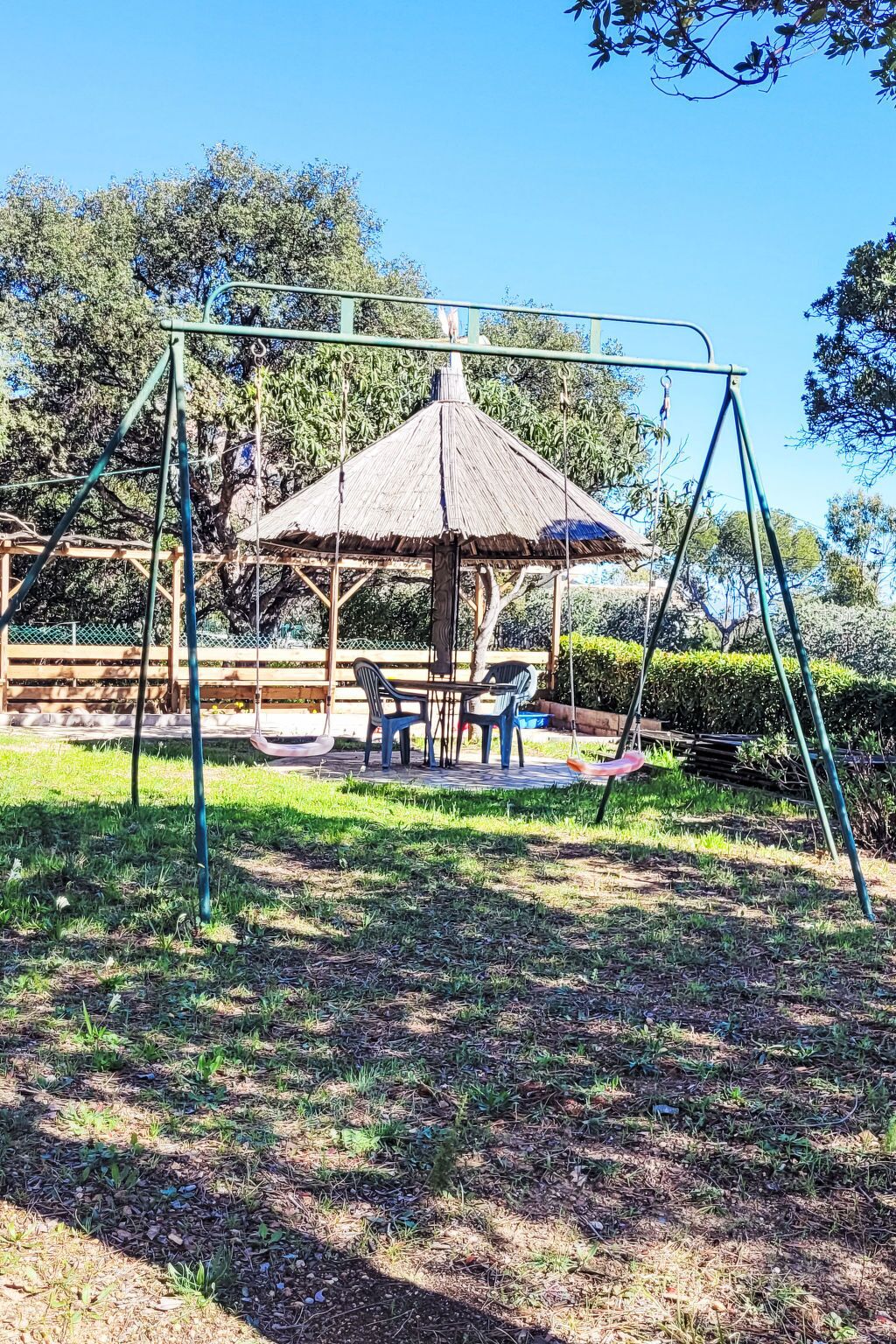 A playground with swings and a table with chairs, surrounded by trees and a grassy area.