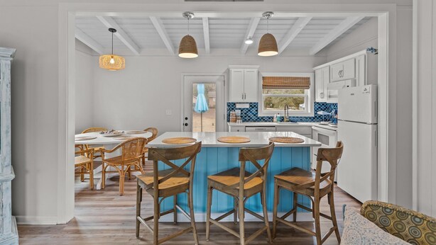 Une cuisine moderne avec des meubles blancs, un îlot central bleu et des chaises en osier.