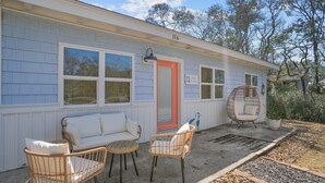 Une maison avec un porche, un canapé blanc, des chaises en osier et une plante en pot.