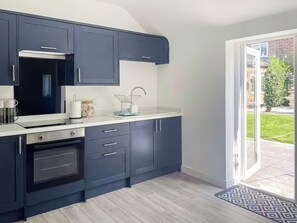 A modern kitchen with dark cabinets, a stainless steel range hood, and a large window overlooking a garden.