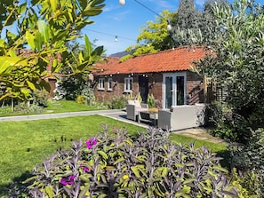 A house with a red-tiled roof, a patio with outdoor furniture, and a well-maintained garden with purple flowers. - 1 bedroom accommodation in Gorefield, near Wisbech (Gorefield, near Wisbech)
