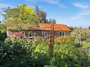 A brick house with a tiled roof surrounded by lush greenery and flowering plants. - 1 bedroom accommodation in Gorefield, near Wisbech (Gorefield, near Wisbech)
