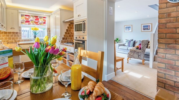 Une cuisine moderne avec des meubles blancs, un four à micro-ondes et un coin repas où une table est dressée pour le petit-déjeuner.