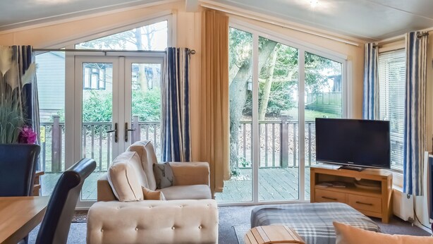 Una stanza con divano, letto, televisore e un balcone che si affaccia su alberi e una recinzione.