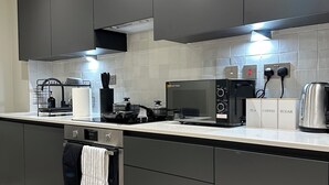 Uma cozinha moderna com armários cinza, exaustor de aço inoxidável, máquina de café e chaleira.