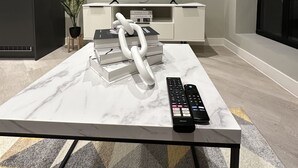 Uma sala de estar moderna com uma mesa de centro de mármore, uma televisão exibindo 'NETFLIX', uma planta e livros.