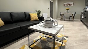 Uma sala de estar moderna com um sofá preto, uma mesa de centro e um espaço de jantar com mesa e cadeiras.