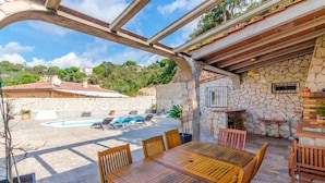 An outdoor patio with a stone wall, wooden table, and chairs. - Awesome home in Vidreres (Vidreres)