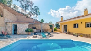 A swimming pool with lounge chairs, a stone wall, and a yellow building with a tiled roof. - Awesome home in Vidreres (Vidreres)